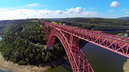 红色的铁桥在绿色的大自然中显得格外耀眼。（视频截图）